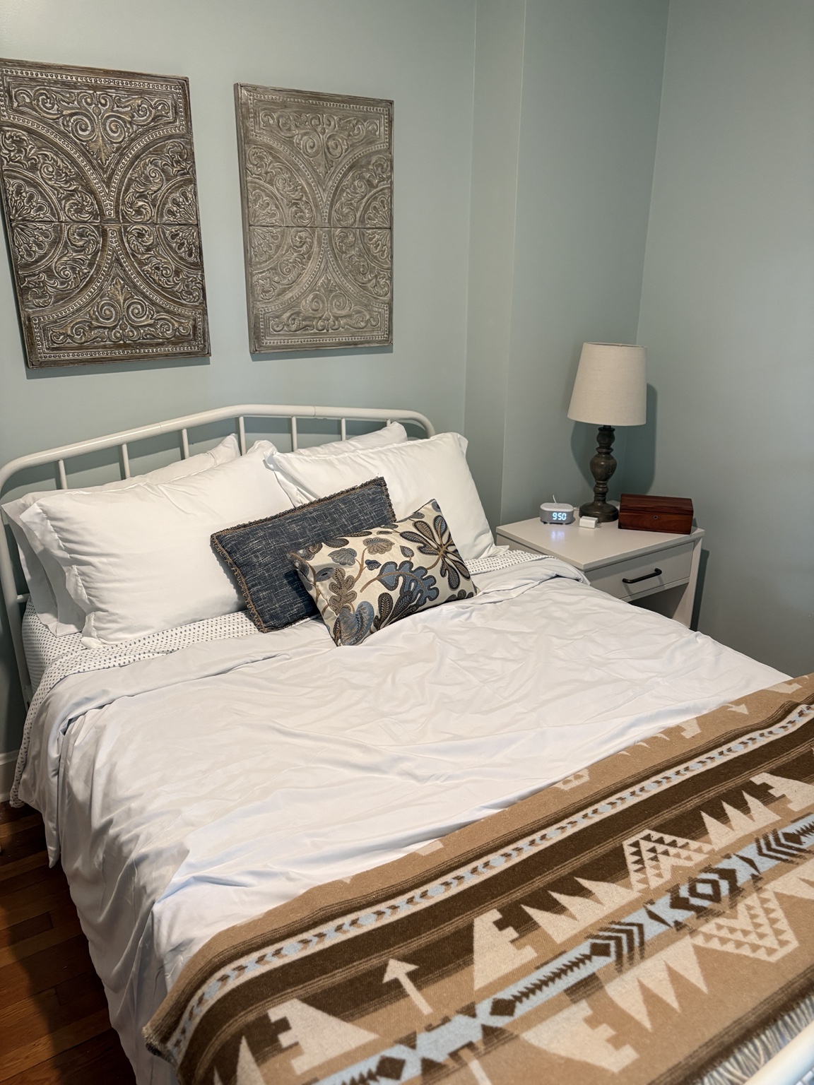 Guest bedroom with a white iron bed, layered blue pillows, and a patterned woven blanket