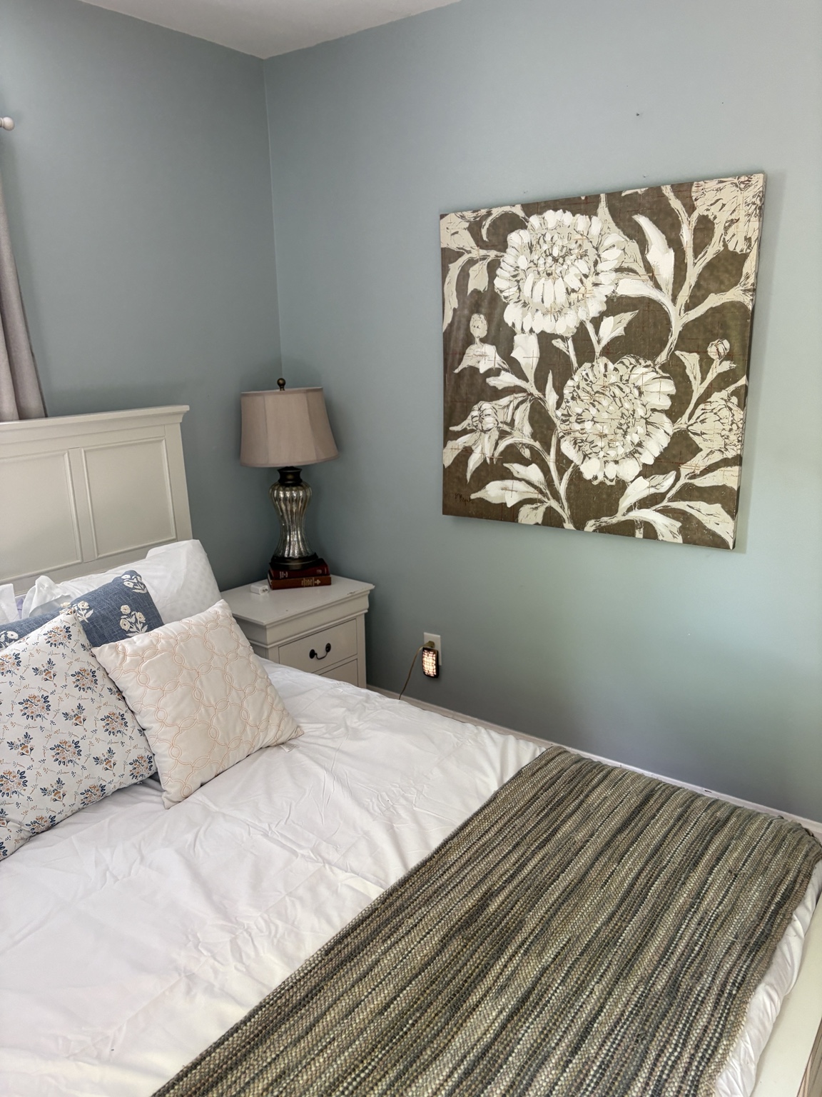 Soft blue bedroom with oversized floral artwork and layered neutral bedding